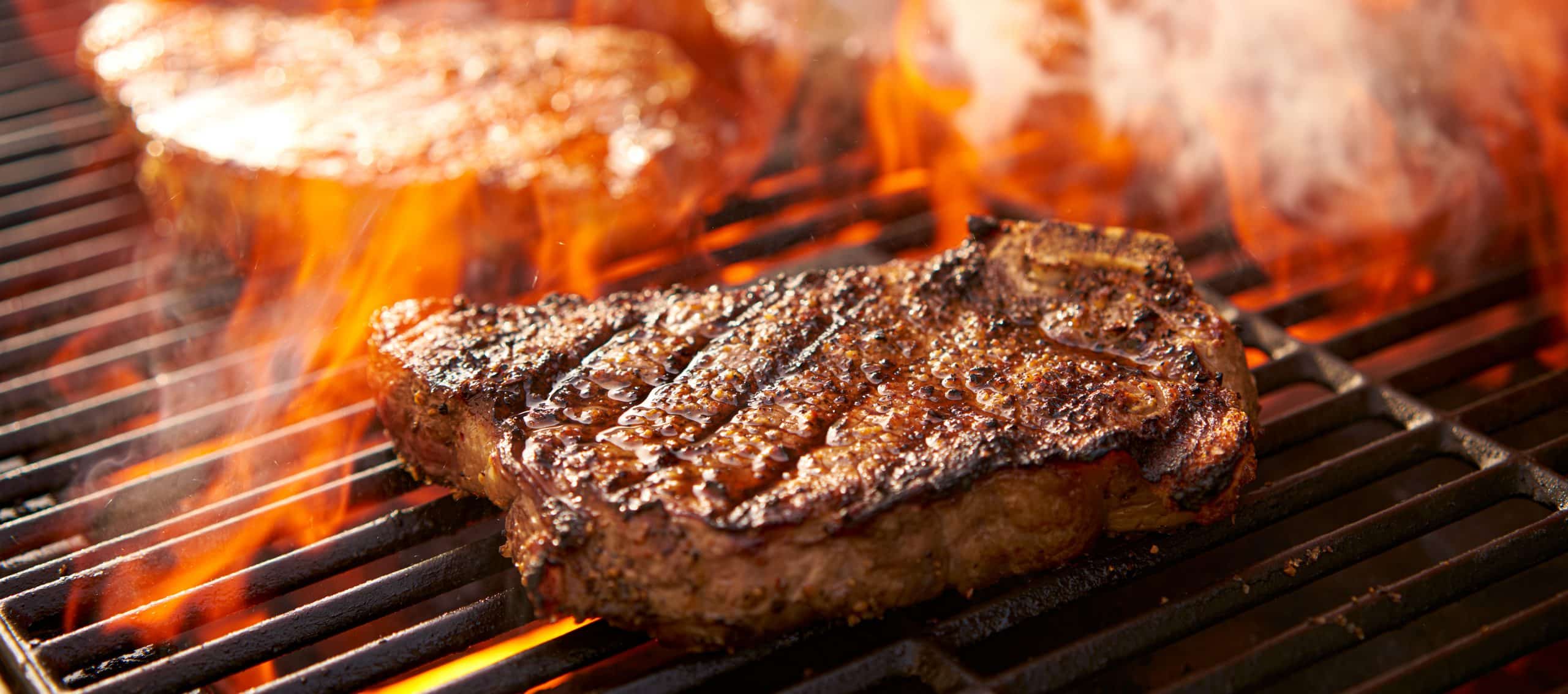 rib eye steaks cooking on flaming grill panorama